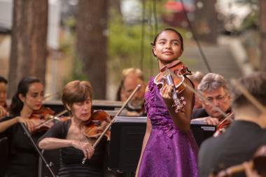 The violin soloist Amaryn Olmeda standing in front of the orchestra smiling