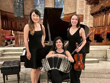 In front of grand piano, pianist and violinist (standing) and bandoneon player (seated in center)