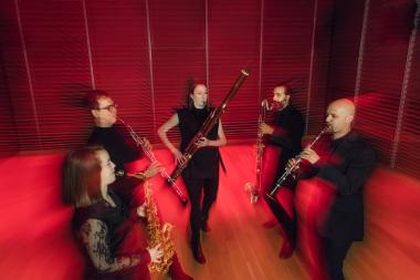 Five musicians playing reed instruments, blurred, in motion, in vivid red lighting