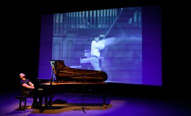 Adam Tendler playing piano in front of a projected image.