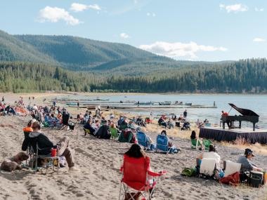 Hunter Noack plays a piano on a beach. The audience is seated on blankets and camp chairs.