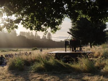 Hunter Noack plays piano in a field with audience members seated in camping chairs while the sun sets