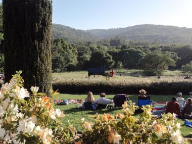 Hunter Noack plays piano in a garden with audience members seated in camping chairs