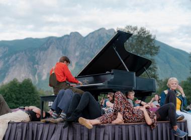 Hunter Noack plays the piano on a stage and audience members surround him and the piano listening to him play