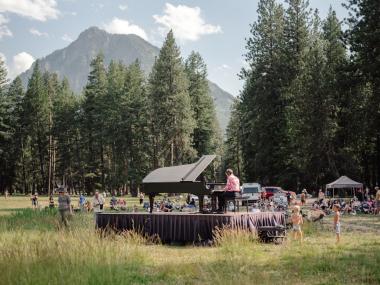 Hunter Noack plays the piano on a stage and audience members surround him and the piano listening to him play