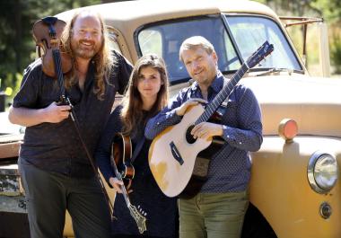 Three musicians with string instruments in front of a vintage truck