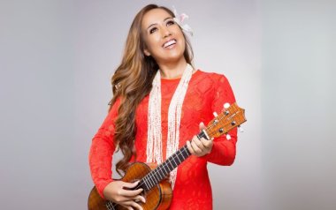 Raiatea Helm in a red dress and pearls with her ukelele.