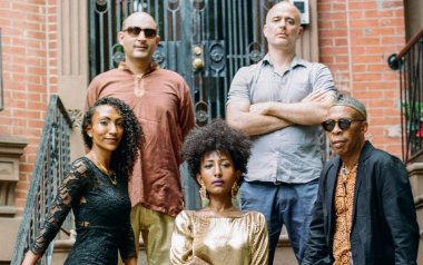 Alsarah & The Nubatones standing together in front of a brick wall.