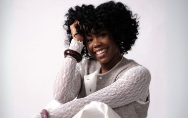 Ekep Nkwelle in a sweater vest and lace top sitting.