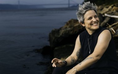 Allison Miller in black on the shore of the ocean.