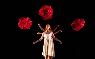 MOMIX dancer in a white dress with three roses around her.