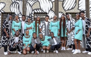 Ndlovu Youth Choir in teal dresses and black and white patterned suits smiling together.