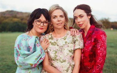 Sara Watkins, Aoife O'Donovan, and Sarah Jarosz standing together in a field.