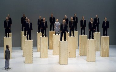 Seventeen Sutra dancers standing on tall wooden blocks with one dancer standing without a block.