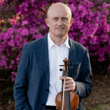 Espen Lilleslåttenen stands with his violin against a background of purple flowers