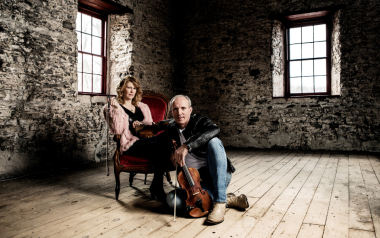 Natalie MacMaster and Donnell Leahy sitting inside an old brick building and holding hands