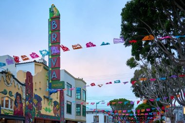 The outside of the Brava Theater at dusk with colorful Day of the Dead paper decorations hung over the street.