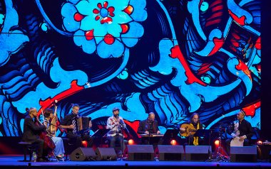 Aga Khan Master Musicians with Vincent Peirani and Vincent Ségal playing in front of a bring blue backdrop
