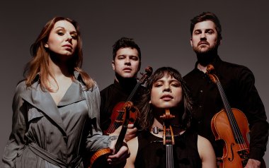 The members of Attacca String Quartet looking into the camera in front of a ombre gray backdrop