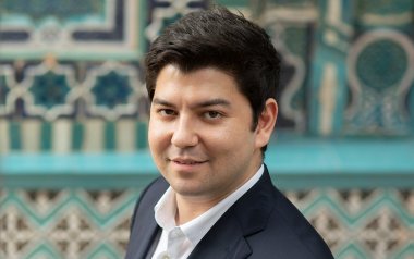 A portrait of Behzod Abdraimov in front of a blue patterned background