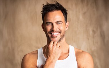 Cheyenne Jackson smiling at the camera in front of a beige background