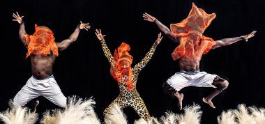 Dancers are jumping with their hands up in front of a black backdrop