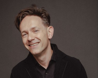 A man smiling at the camera in front of a gray background.