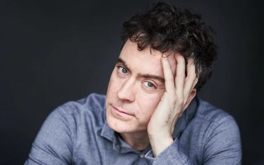 A portrait of Paul Lewis. He is wearing a navy shirt and is posing in front of a black background