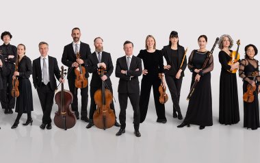 The English Concert holding their instruments in front of a white back drop