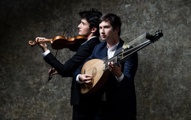 Portrait of Théotime Langlois de Swarte and Thomas Dunford holding their respective instrument in front of a gray back drop