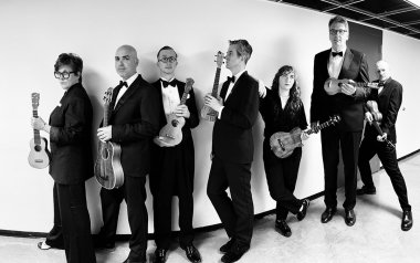 A black and white photo of the Ukulele Orchestra of Great Britain holding their ukulele 