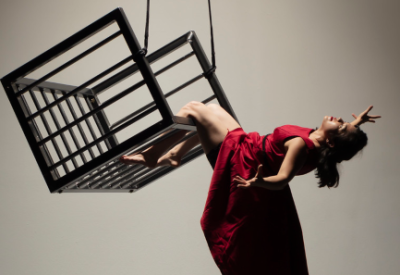Female dancer in red dress hanging from cage