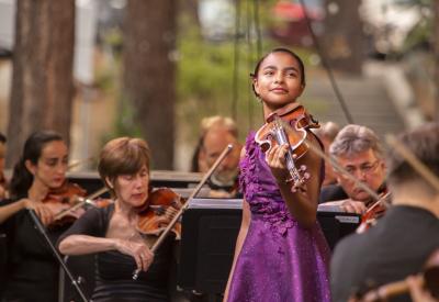 The violin soloist Amaryn Olmeda standing in front of the orchestra smiling