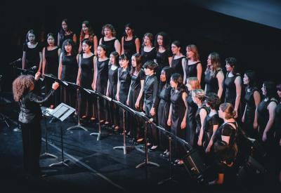 The San Francisco Girls Chorus on a dark stage, being conducted by Valérie Sainte-Agathe