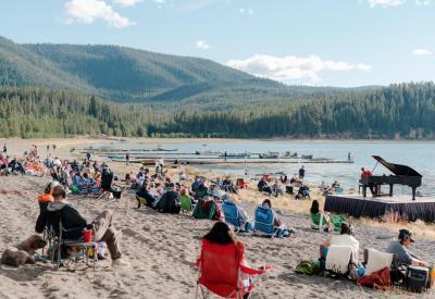 Hunter Noack plays a piano on a beach.  The audience is seated on blankets and camp chairs.