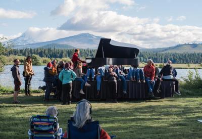 Hunter Noack plays the piano on a stage and audience members surround him and the piano listening to him play