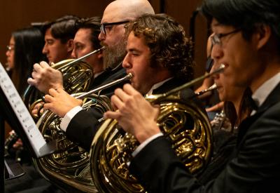 A closeup of four brass French horn players of the UC Davis Symphony Orchestra in concert black attire (Phil Daley/UC Davis)