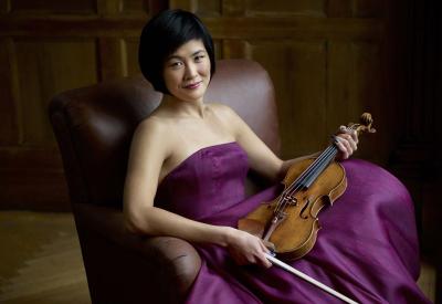 Jennifer Koh in a purple dress relaxing in a chair, holding her violin and bow