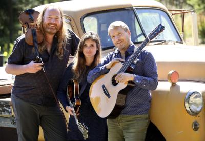 Three musicians with string instruments in front of a vintage truck