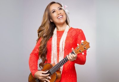 Raiatea Helm in a red dress and pearls with her ukelele.