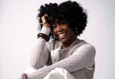Ekep Nkwelle in a sweater vest and lace top sitting.