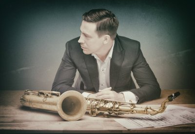 Håkon Kornstad in a suit sitting behind a saxophone and sheet music. 