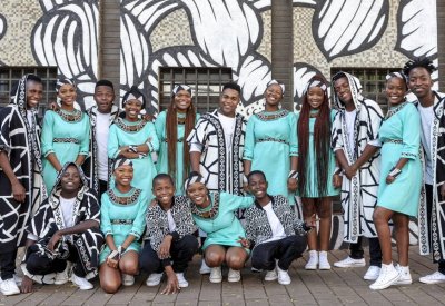 Ndlovu Youth Choir in teal dresses and black and white patterned suits smiling together.