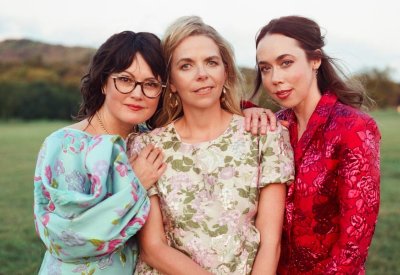 Sara Watkins, Aoife O'Donovan, and Sarah Jarosz standing together in a field.