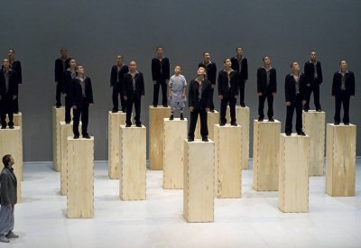 Seventeen Sutra dancers standing on tall wooden blocks with one dancer standing without a block.