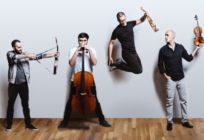 The members of Invoke Quartet are posing with their instruments against a white wall