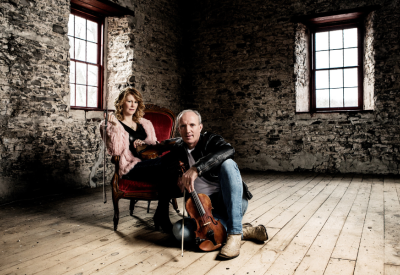 Natalie MacMaster and Donnell Leahy sitting inside an old brick building and holding hands