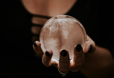 A woman's torso, dressed in black, and holding a crystal ball