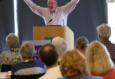 Instructor Scott Foglesong stands behind lecture stand with arms up in front of class.