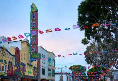 The outside of the Brava Theater at dusk with colorful Day of the Dead paper decorations hung over the street.